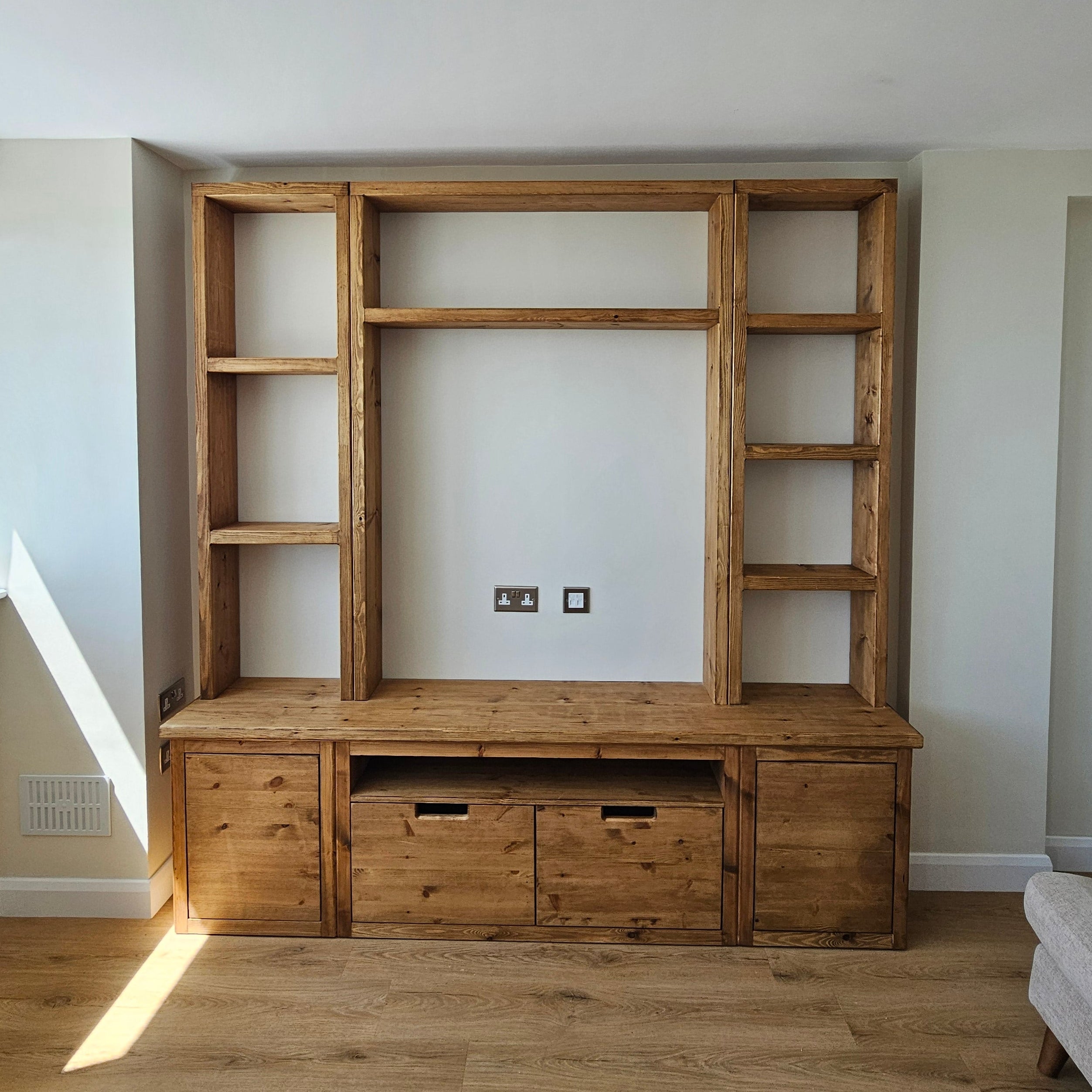 A rustic wooden built-in shelving unit and cabinet system mounted on a white wall in a home interior, shown from an angled overhead perspective.